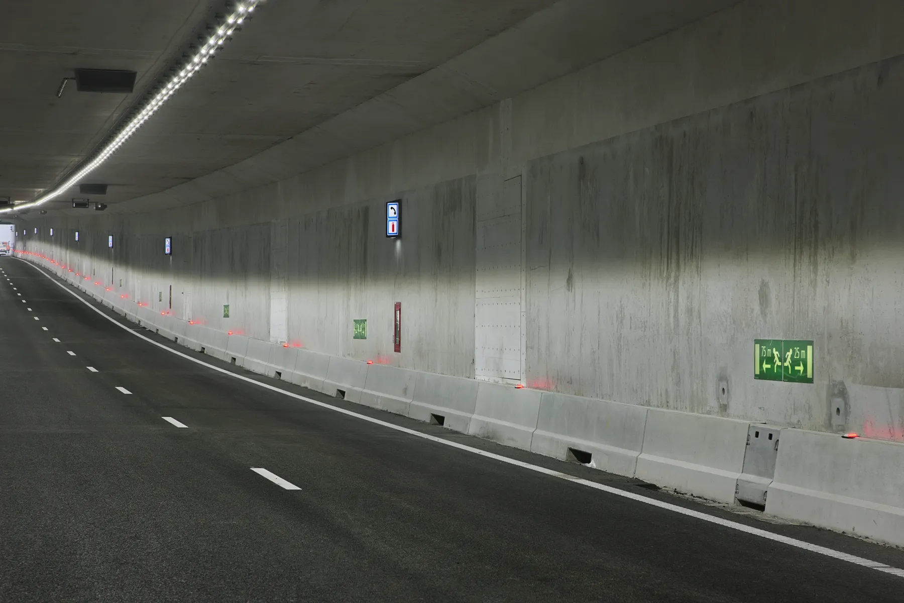 Tunnelbuis met verlichte vluchtweg- en hulppostborden langs de wand
